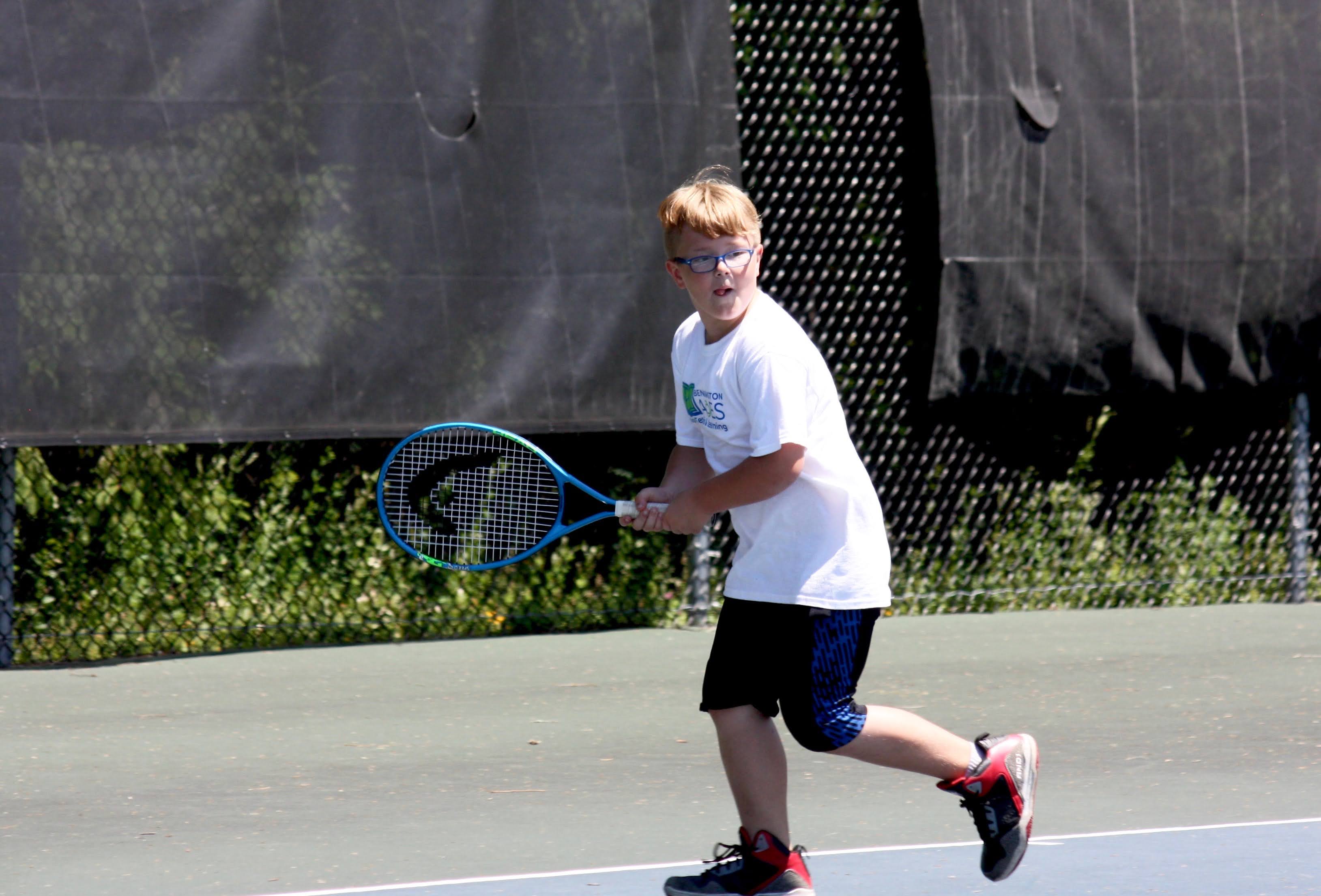 A small boy playing tennis ball in a coat